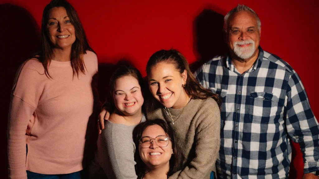 A multi-generational family smiling together against a plain red studio background.