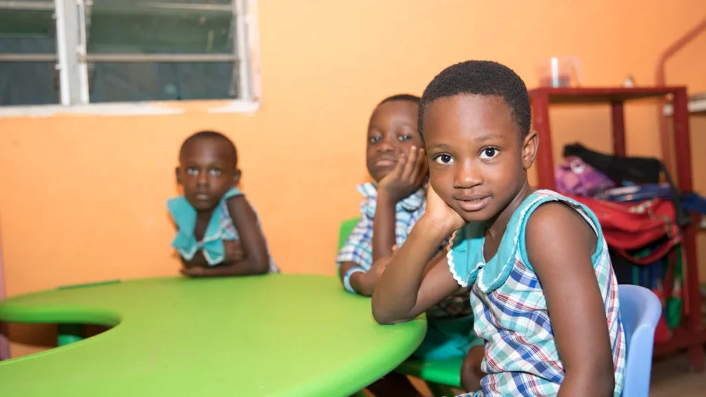 Young children sitting at a vibrant green classroom table, focusing on creative activities.