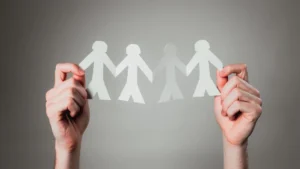 Two hands holding a cut-out paper chain of human figures symbolizing community unity and togetherness.