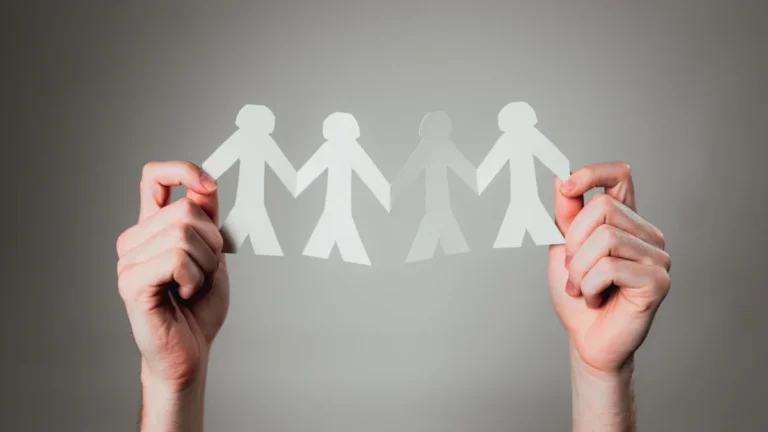 Two hands holding a cut-out paper chain of human figures symbolizing community unity and togetherness.