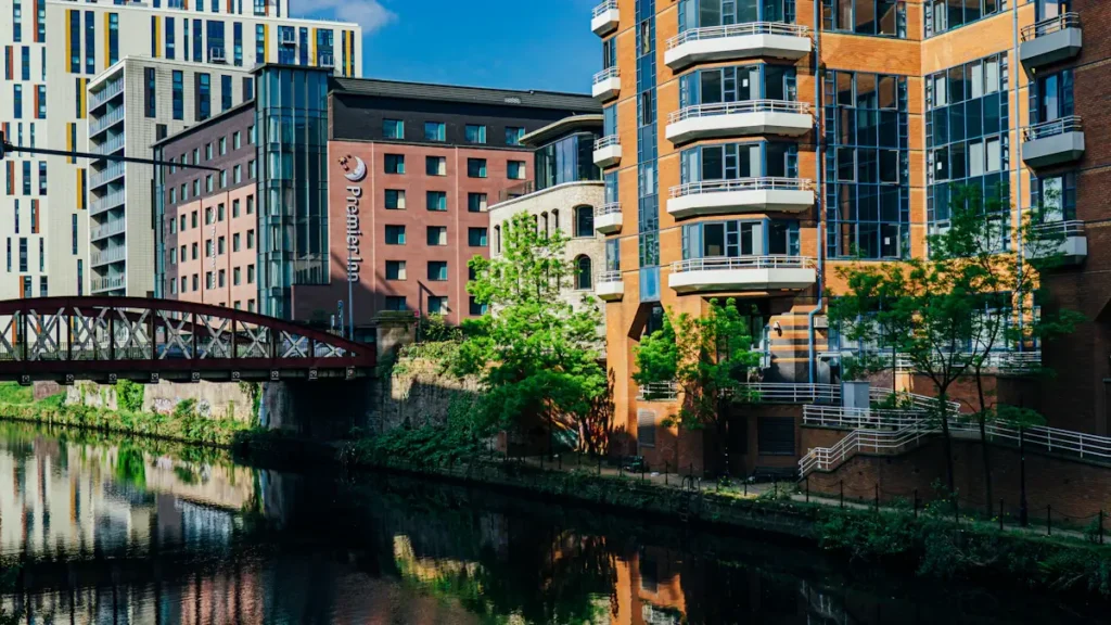 Modern buildings reflecting on a Manchester canal waterway during the day.