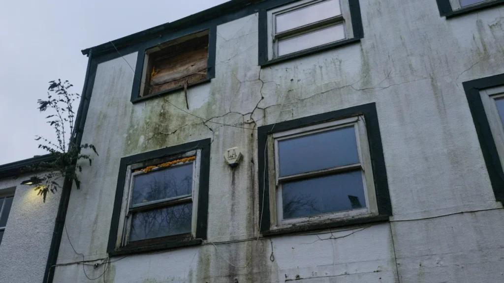 An old, weathered apartment building in England with multiple boarded-up windows.