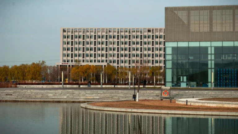 Contemporary glass buildings reflecting in a calm pool of water under a clear sky.