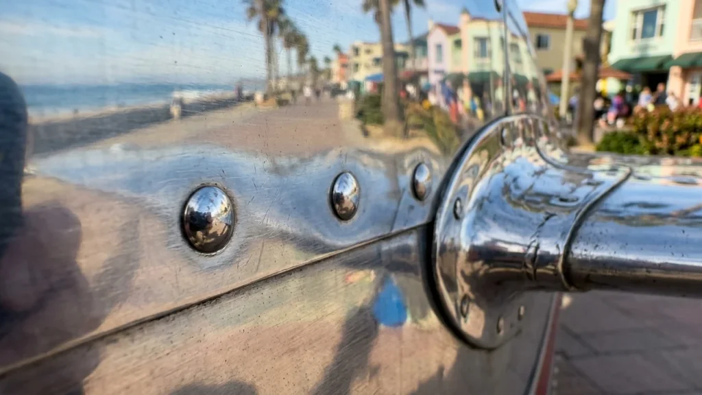 Close-up of a polished metal surface reflecting a blurry beach boardwalk and coastal town.