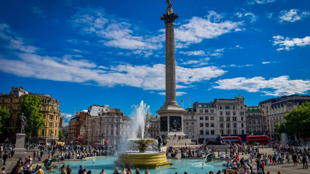 Crowds gathering around the Trafalgar Square fountain in central London on a sunny day.