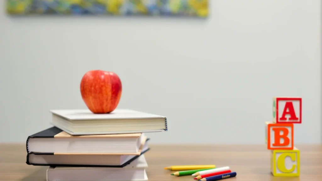 Red apple resting on a stack of books with alphabet blocks on desk.