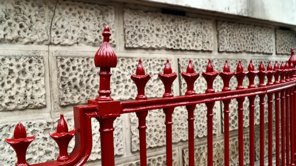 Close-up of freshly painted red cast-iron railings against a stone wall.