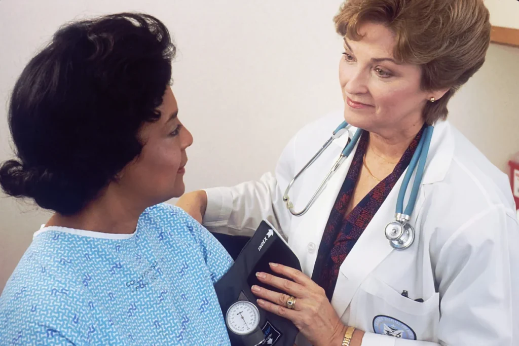 A female doctor in a white coat measures a female patient's blood pressure.