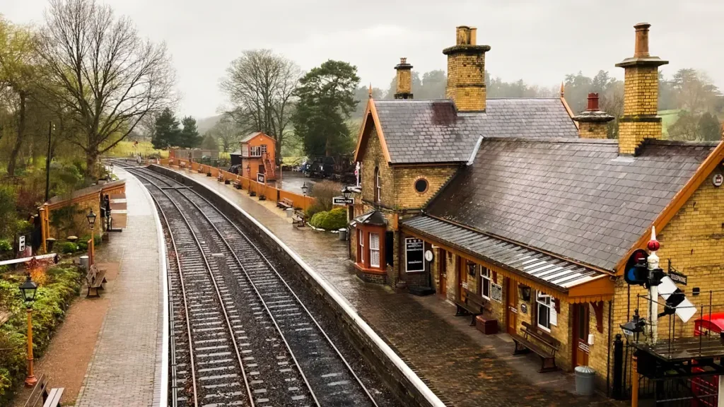 An empty, traditional-style British train station platform with tracks and historic brick buildings.