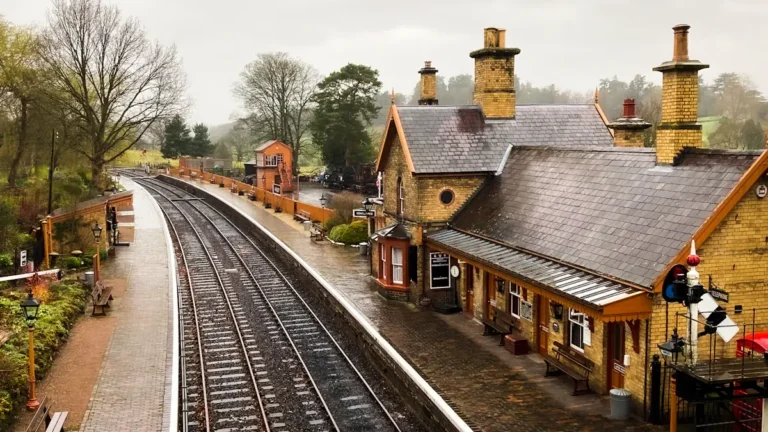 An empty, traditional-style British train station platform with tracks and historic brick buildings.