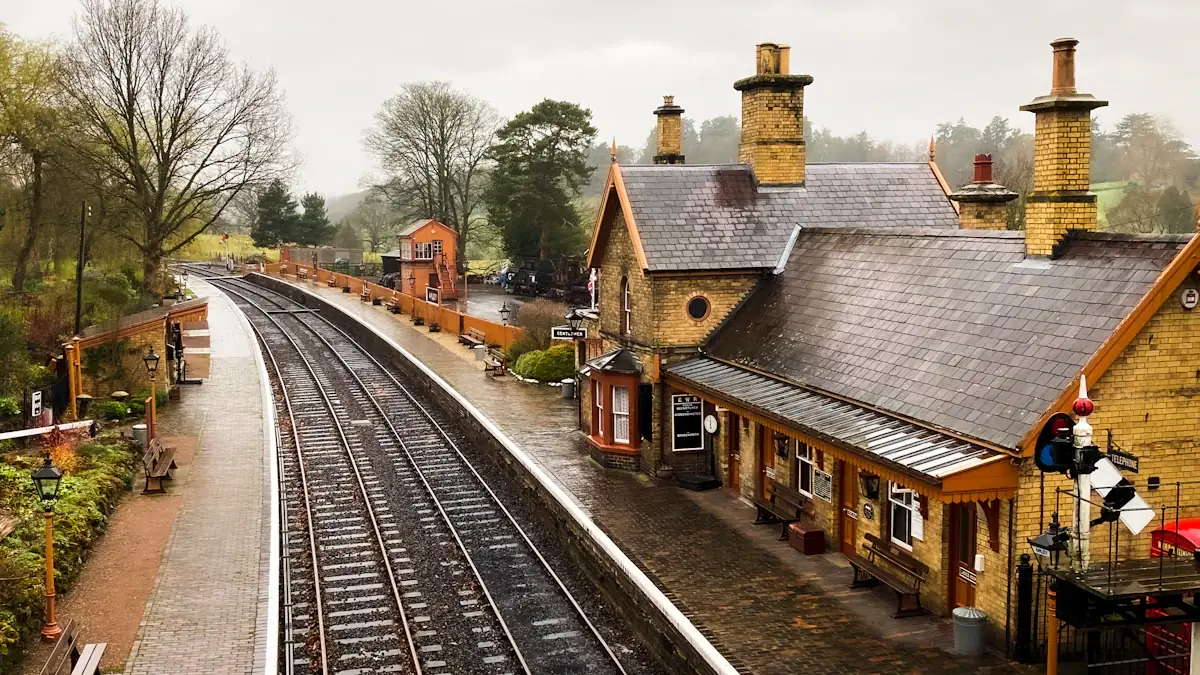 An empty, traditional-style British train station platform with tracks and historic brick buildings.