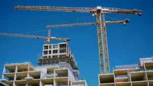 Modern high-rise residential apartment building under construction with tall cranes against clear sky.