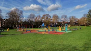 Colorful playground equipment in a lush green London park on a sunny day.