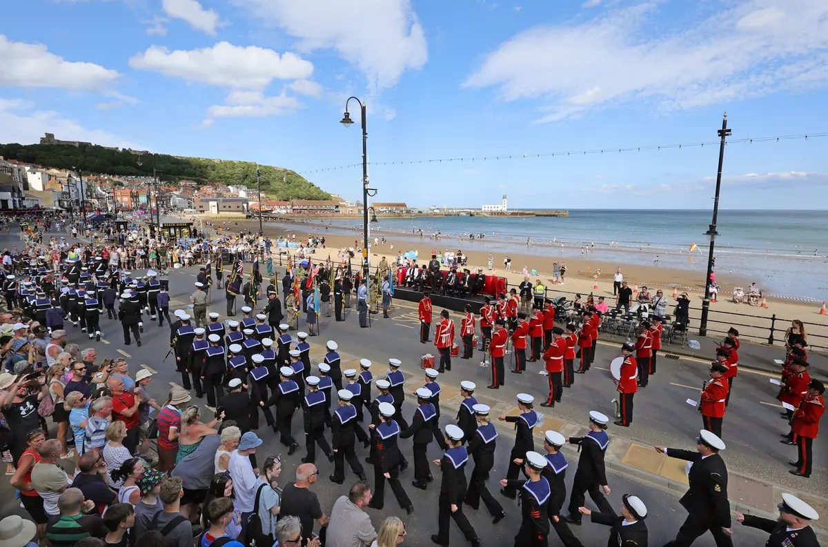 Military parade with marching bands and personnel in uniform on a coastal promenade