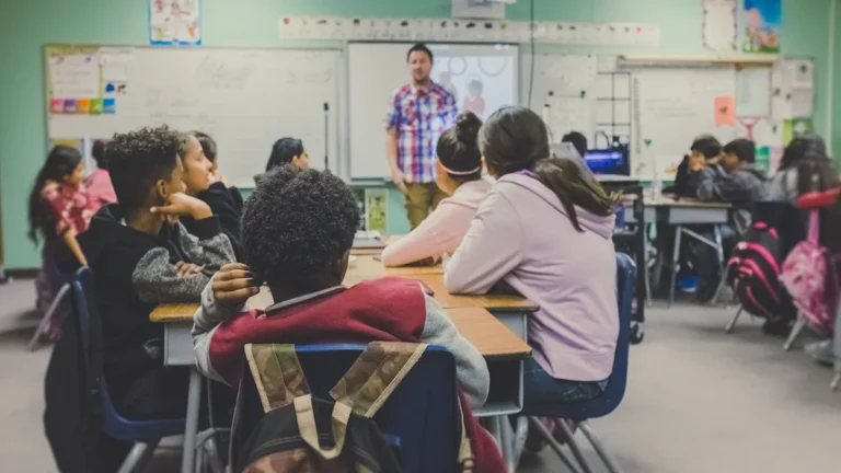 Students in a classroom setting listening to a teacher during a lesson.