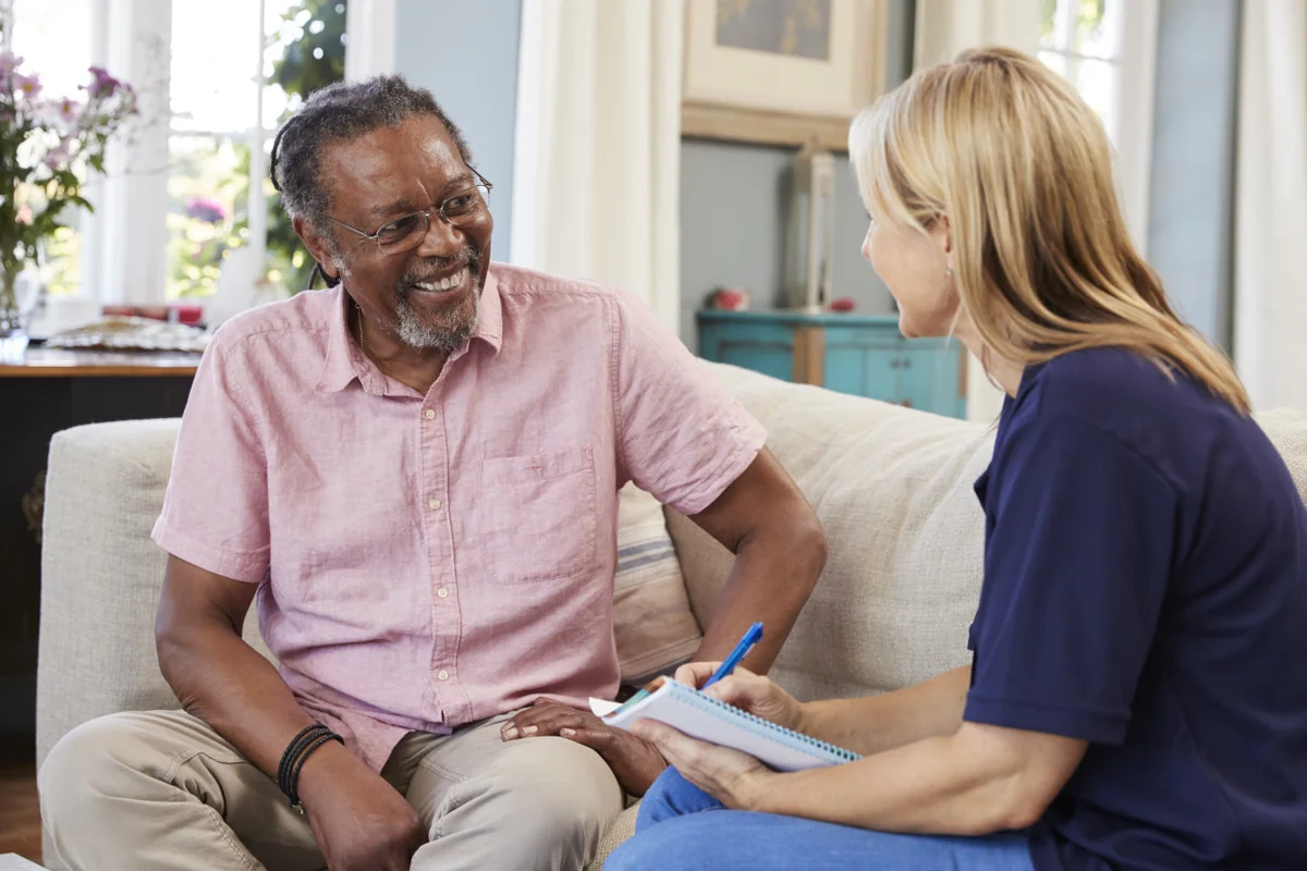 An older man with glasses smiling while talking to a female home healthcare worker.
