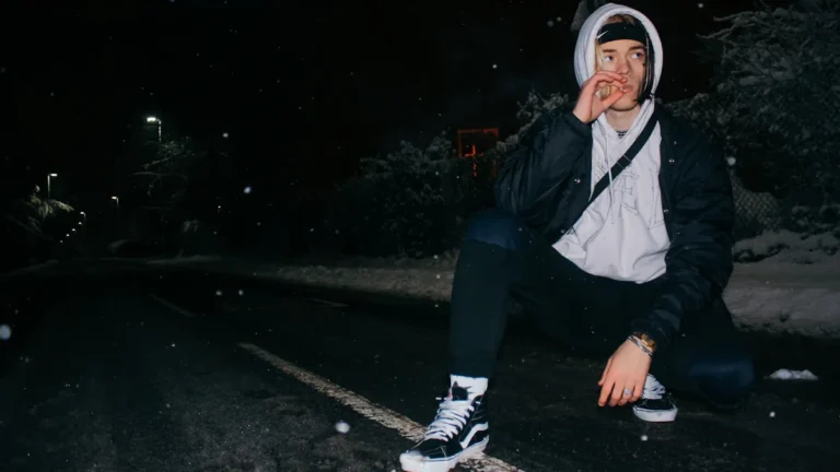 A person crouching on a snowy road at night in the West Midlands.