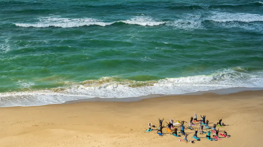 A small group of people practicing yoga on a sandy UK beach.
