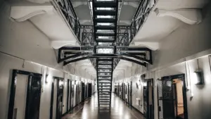 An atmospheric, dimly lit prison hallway with lights casting shadows on the floor.