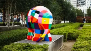A colorful Elmer the Elephant sculpture standing on a concrete plinth in a park.