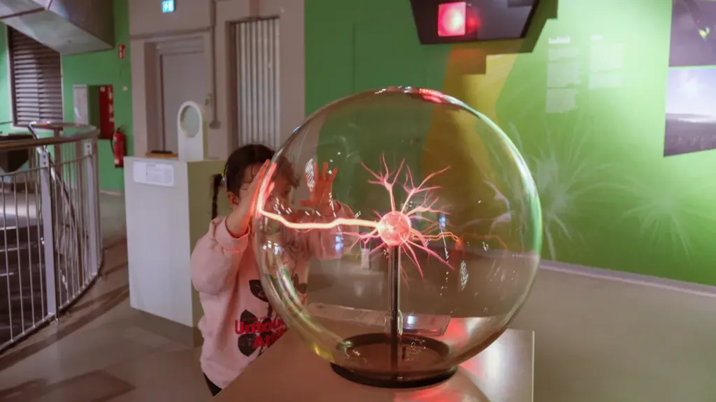 A child touches a glowing plasma ball in an interactive science museum exhibit.