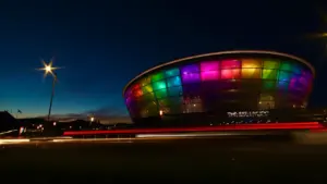 The OVO Hydro arena in Glasgow illuminated at night with vibrant multi-colored lights.