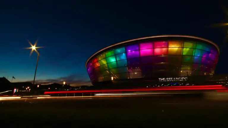 The OVO Hydro arena in Glasgow illuminated at night with vibrant multi-colored lights.