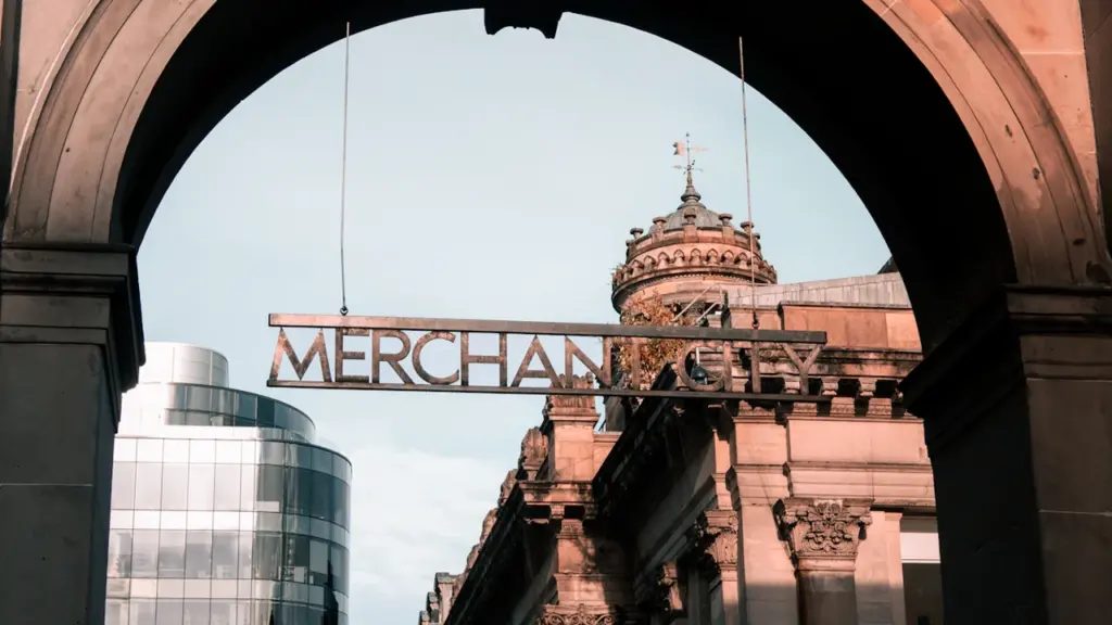 The Merchant City sign suspended under a stone archway in Glasgow, Scotland.