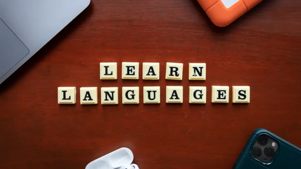 Scrabble tiles spelling out Learn Languages on a table with digital devices.