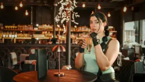 A woman dressed as Lara Croft drinks from a glass inside a dimly lit bar.