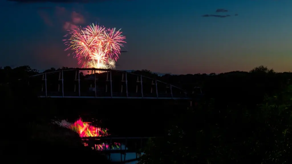 Vibrant fireworks illuminate the night sky above a historic British suspension bridge at dusk.
