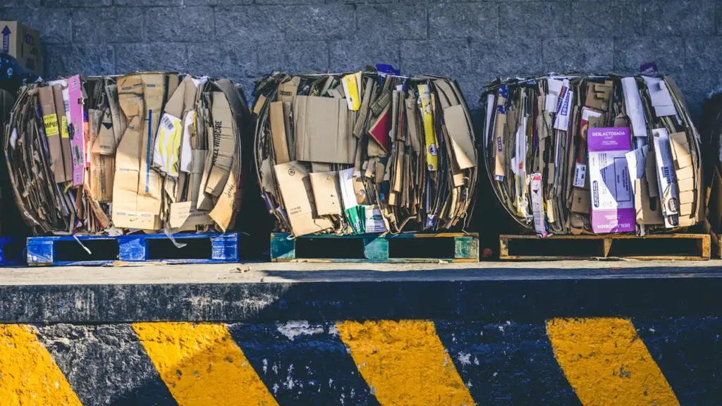 Large compressed cardboard bales stacked on wooden pallets at an industrial site.