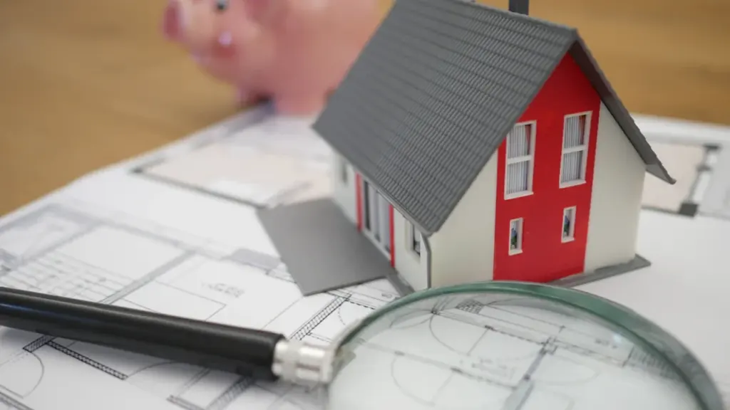 Model house and magnifying glass placed on top of housing floor plans