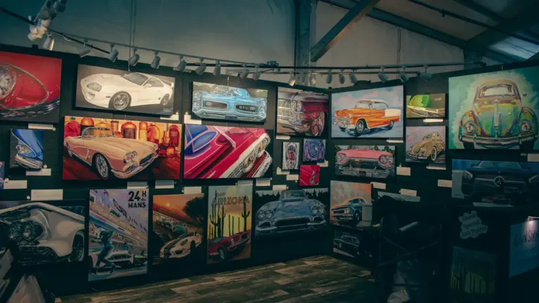 A gallery wall displaying various automotive artworks at an indoor exhibition hall.