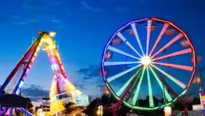 Brightly illuminated ferris wheel and carnival ride at a summer fair at night.