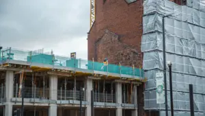 A large crane hovering over a brick building wrapped in construction scaffolding