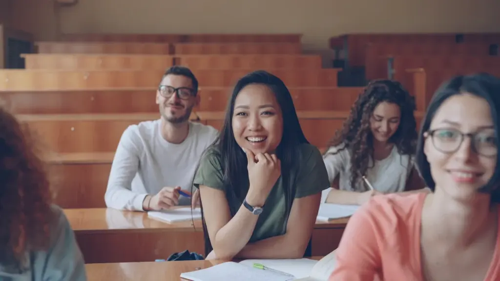 Students sitting at desks in a university lecture hall looking towards the camera.
