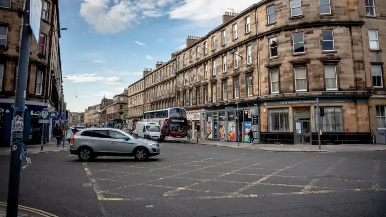 Street view of a busy Edinburgh intersection with historic stone buildings and a bus.