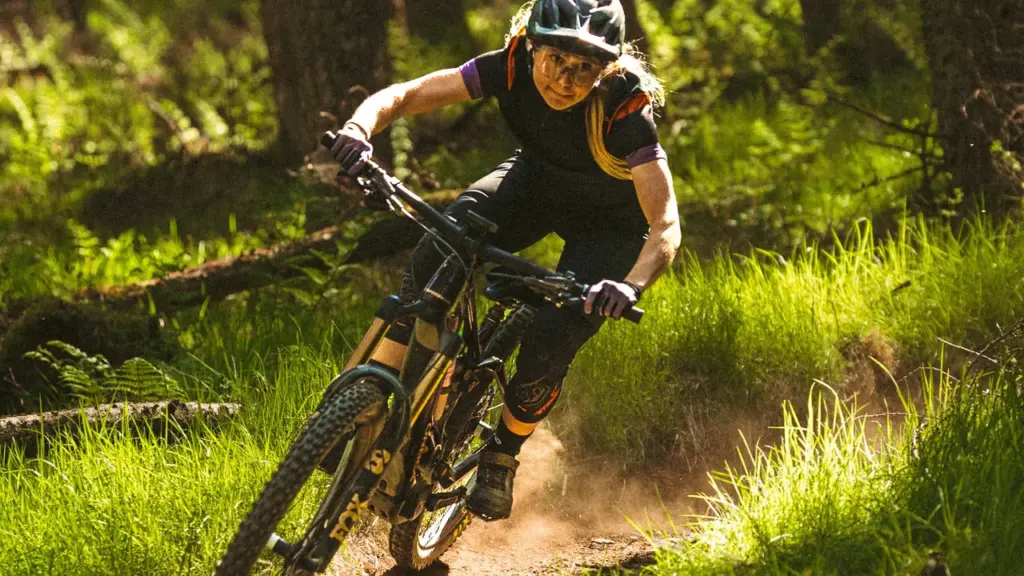 A female mountain biker rides her bike quickly along a sunlit dirt forest trail.
