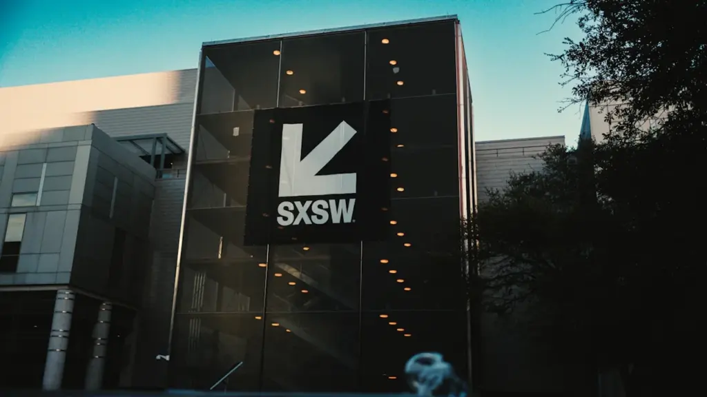 Modern glass building exterior with a large logo under a clear blue sky.
