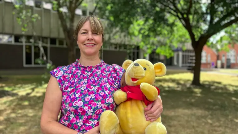 A smiling woman wearing a floral top holds a plush Winnie the Pooh bear.