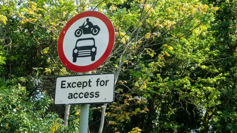 UK road sign prohibiting motor vehicles surrounded by lush green trees and foliage
