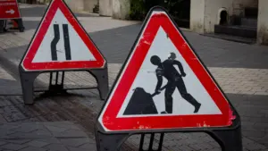Two triangular road construction signs stand on a paved street during city road work.