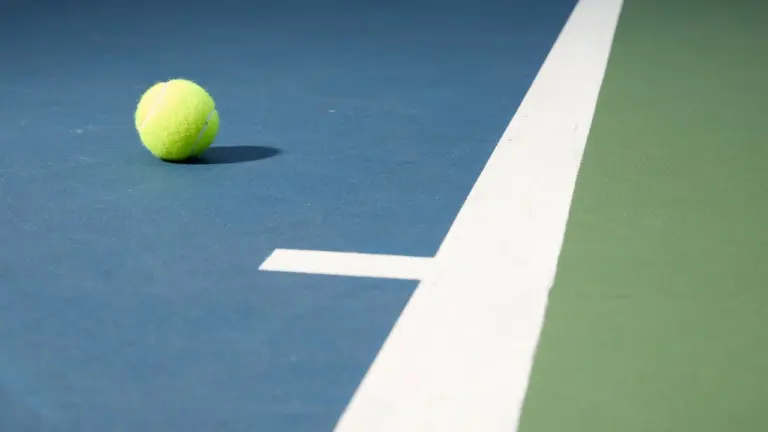 A single bright yellow tennis ball resting on a blue and green tennis court.