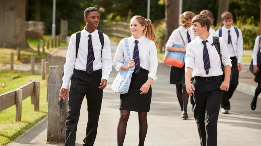 A group of teenage students in formal uniforms walking together outdoors on campus.
