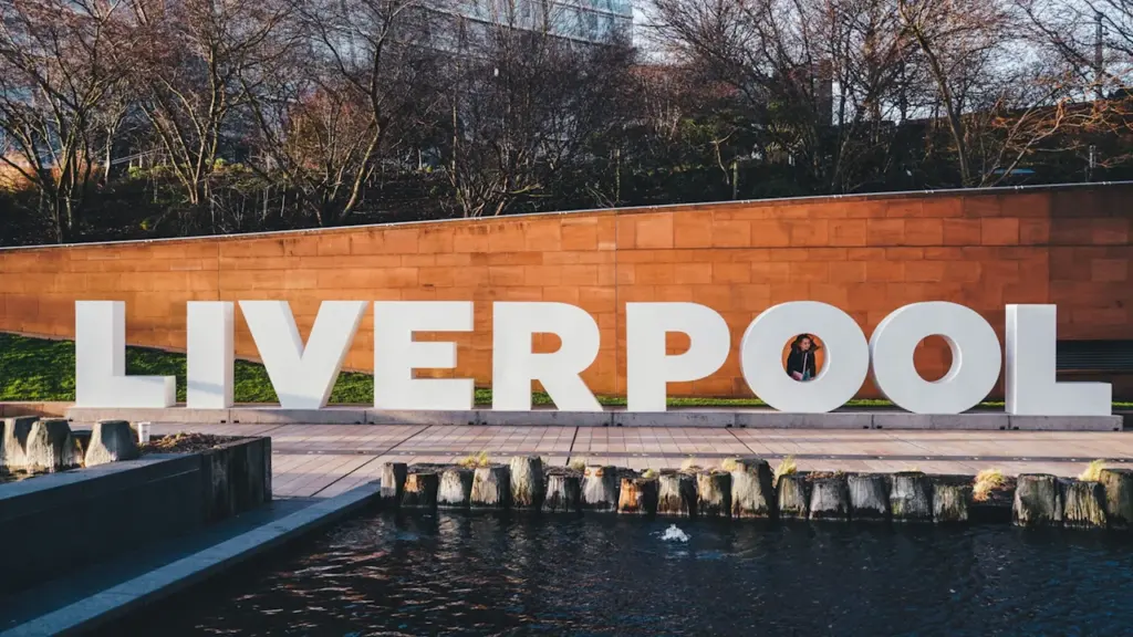 Large white LIVERPOOL sign positioned by a reflective water feature outdoors in Liverpool.