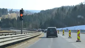Traffic light signals at a highway construction zone with trees in the background.