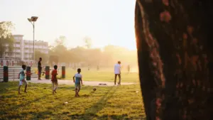 Children playing sports on a grass field during a sunny summer evening.