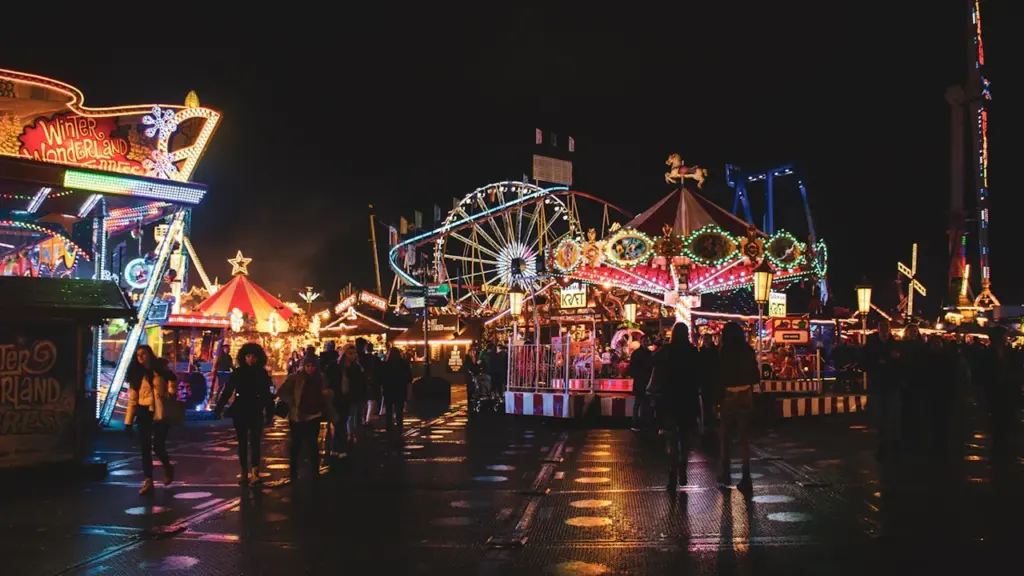 Vibrant fairground rides illuminated at night in a bustling amusement park setting.