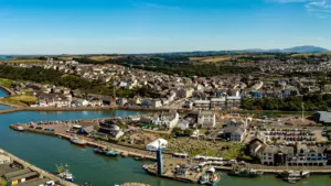 Aerial view of a coastal town harbor with boats and a busy public park.